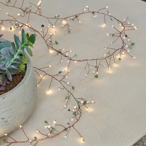 Puede incluir: Luces de hadas de alambre de cobre con cuentas blancas y verdes. Las luces están enhebradas en un alambre con forma de rama y son perfectas para agregar un toque de fantasía a cualquier espacio.