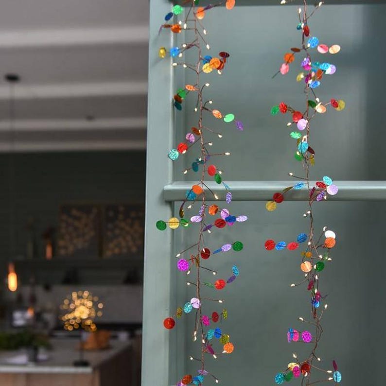 Puede incluir: Dos guirnaldas de luces de alambre de cobre con peque&ntilde;as lentejuelas circulares multicolores en tonos rojo, azul, verde, naranja y morado. Los cables finos y flexibles est&aacute;n iluminados por diminutas bombillas LED de luz blanca c&aacute;lida.