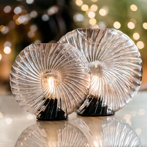 May include: Two clear glass table lamps with a spiral design. The lamps have a black base and are lit with a warm white light.