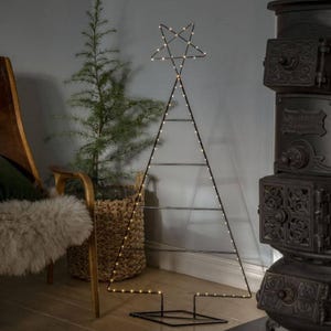 May include: A tall, triangular wire frame shaped like a Christmas tree, constructed from thin black metal. The frame is outlined with small, glowing warm white LED lights and topped with a five-pointed star, standing on a flat base.