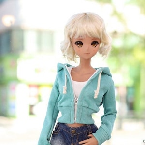 May include: A fashion doll wearing a teal hoodie, denim shorts, and sneakers. The doll has blonde hair and is standing in front of a window. A miniature sailboat and other decorative items are on display.