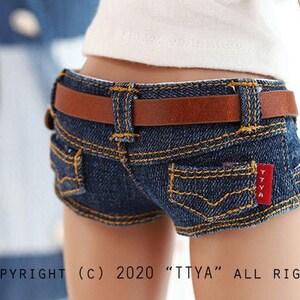 May include: A pair of denim shorts with a brown leather belt. The shorts have a red label with the text "TTYA" on the back pocket.