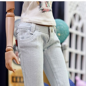 May include: Light blue denim jeans with a straight leg fit. The jeans are shown on a doll wearing yellow sneakers with white laces.