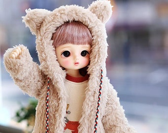 May include: A doll wearing a tan teddy bear hooded jacket, a cream-colored sweater with a red graphic, gray and white striped leggings, and black boots. The doll has a fair complexion and pink hair. The image includes the text "COPYRIGHT (C) 2019 'TTYA' ALL RIGHTS RESERVED."