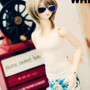 May include: A doll wearing a white tank top and blue and white floral pants. The doll is wearing sunglasses and has long blonde hair. The doll is standing in front of a red cabinet with the words "Home Sweet Home" on it. The doll is holding a small toy house in her hand.