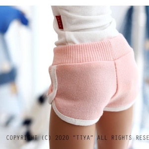 May include: Pink athletic shorts with white trim. The shorts have a ribbed waistband and are made of a soft, textured fabric.