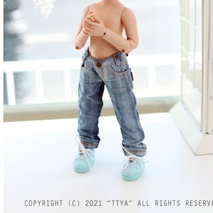 May include: A doll with brown hair in pigtails wearing blue jeans and light blue sneakers. The doll is standing in front of a white window.