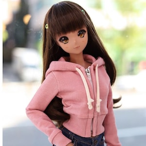 May include: A doll with long brown hair, wearing a pink hooded sweatshirt and denim shorts. The sweatshirt has a zipper and white drawstrings. The doll has large eyes and is wearing small hair clips. The image includes the text "COPYRIGHT (C) 2021 "TTYA" ALL RIGHTS RESERVED."