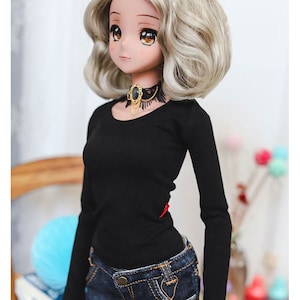 May include: A doll with blonde hair wearing a black long-sleeved shirt and blue jeans. The doll is wearing a black choker with a gold chain and a black gemstone.