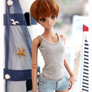 May include: A doll with brown hair wearing a gray tank top and light blue denim shorts. The doll is standing in front of a blue and white striped background.