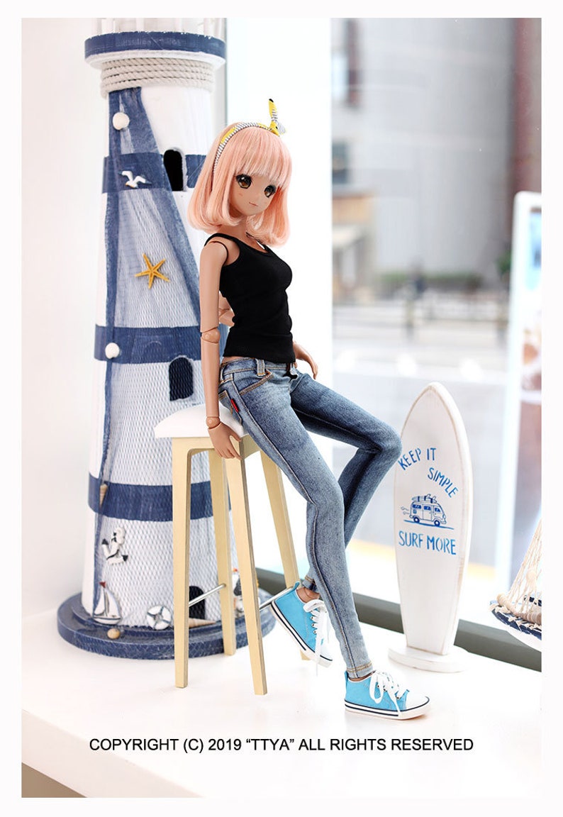 Puede incluir: Una mu&ntilde;eca con un top negro sin mangas, jeans azules y zapatillas azules est&aacute; sentada en un taburete de madera. La mu&ntilde;eca tiene el pelo largo y rosa y lleva una diadema amarilla. En el fondo hay una tabla de surf blanca con el texto "Keep it simple, surf more".