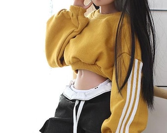 May include: A yellow cropped sweatshirt with white stripes on the sleeves. The sweatshirt has a relaxed fit and is made of a soft, comfortable fabric.