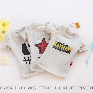 May include: Three gray t-shirts with different graphic designs. The designs include a red star, a black and white hashtag, and a yellow "Batman" logo.