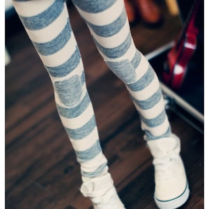 May include: A pair of white and blue striped leggings with knee patches. The leggings are worn with white sneakers.