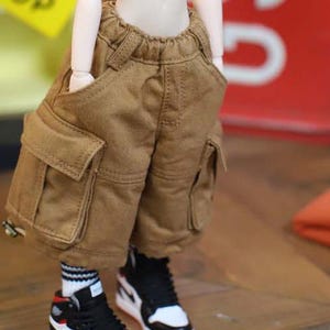 May include: Brown cargo shorts with large side pockets and an elastic waistband. The shorts are worn with black and white sneakers with red accents and white socks with black stripes. The shorts are made of a durable fabric.