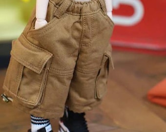 Puede incluir: Pantalones cortos cargo marrones con grandes bolsillos laterales y cintura elástica. Los pantalones cortos se combinan con zapatillas deportivas negras y blancas con detalles rojos y calcetines blancos con rayas negras. Los pantalones cortos son de tela resistente.