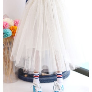 K&ouml;nnte beinhalten: Ein wei&szlig;er T&uuml;llrock mit einem goldenen Glitzerbund. Der Rock ist geschichtet und hat eine flie&szlig;ende Silhouette.