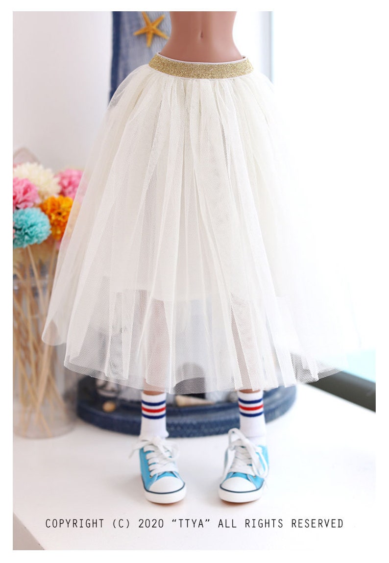 K&ouml;nnte beinhalten: Ein wei&szlig;er T&uuml;llrock mit einem goldenen Glitzerbund. Der Rock ist geschichtet und hat eine flie&szlig;ende Silhouette.