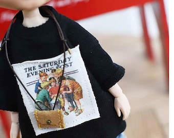 Puede incluir: Una camiseta negra con un parche blanco con el texto "THE SATURDAY EVENING POST" y una ilustración de niños. Un pequeño bolso marrón cuelga de una correa alrededor del cuello.