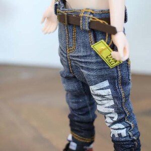 Può includere: Jeans blu con cintura marrone ed etichetta gialla. I jeans hanno un testo bianco sulla gamba che recita "VINTAGE". I jeans hanno cuciture gialle e sono risvoltati alle caviglie.