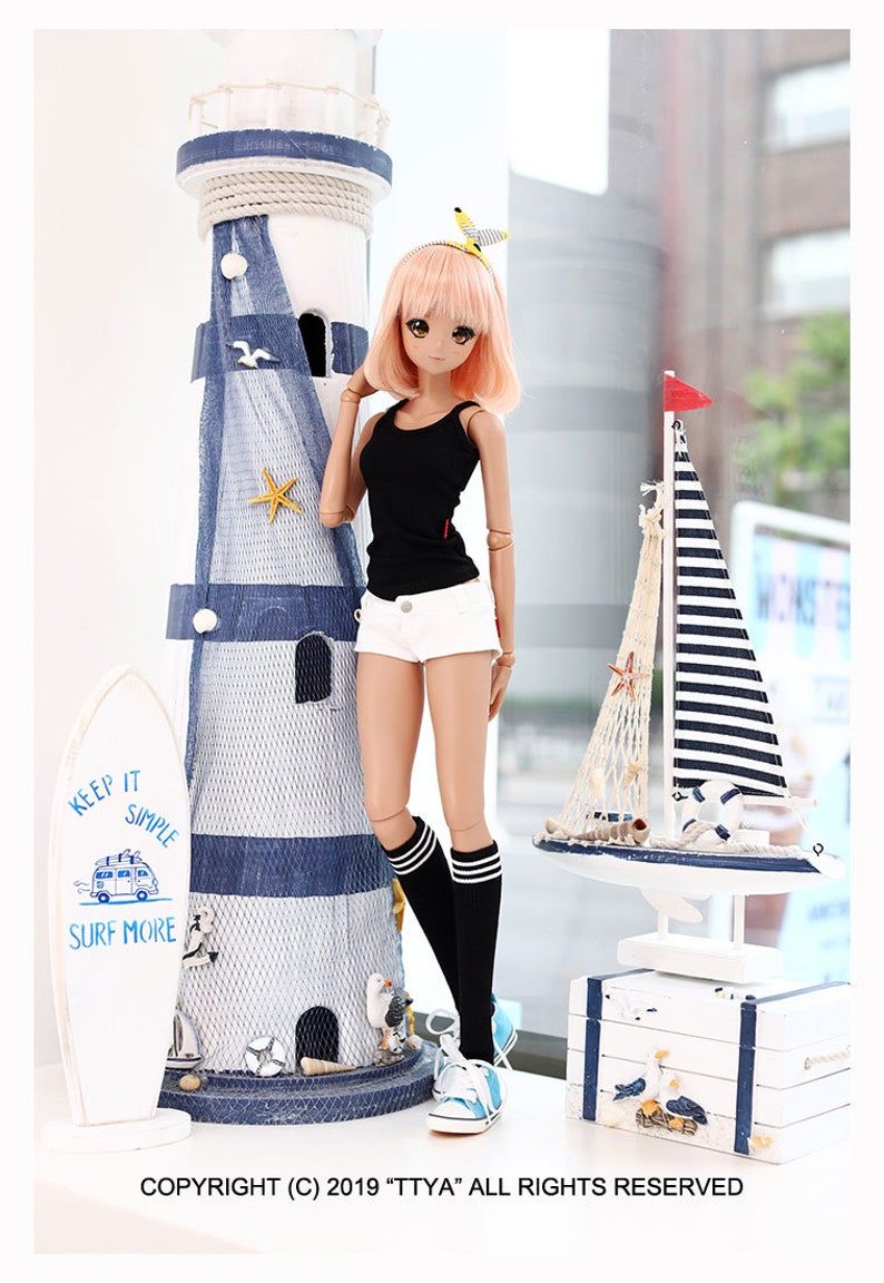 Puede incluir: Una mu&ntilde;eca con el pelo rosa que lleva un top negro sin mangas, pantalones cortos blancos, calcetines a rayas blancas y negras y zapatillas azules. La mu&ntilde;eca est&aacute; de pie junto a un faro blanco con rayas azules y blancas y una tabla de surf blanca con el texto "Keep it simple, surf more".