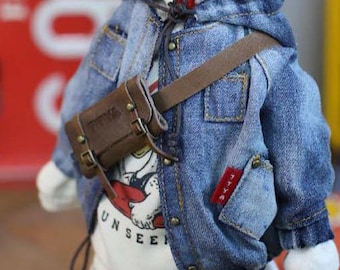 Puede incluir: Una chaqueta vaquera azul con un bolso bandolera de cuero marrón. La chaqueta tiene botones y bolsillos. Una camiseta blanca con la palabra "UNSEEN" es visible debajo de la chaqueta.