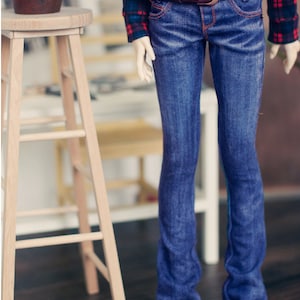 May include: A doll wearing a red and black plaid shirt with a brown belt and blue denim jeans.