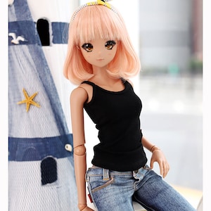 Puede incluir: Una mu&ntilde;eca con el pelo rosa que lleva un top negro sin mangas y unos vaqueros azules. La mu&ntilde;eca est&aacute; sentada en un taburete blanco. La mu&ntilde;eca lleva una diadema amarilla y blanca con un lazo en la parte superior.