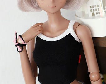 May include: A doll wearing a black and white tank top with a white trim. The doll has long, straight, light pink hair and brown eyes.