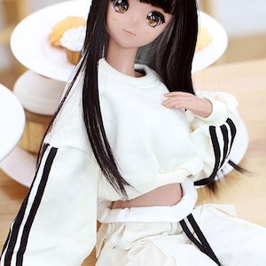 May include: A white cropped sweatshirt with black stripes on the sleeves. The sweatshirt is worn by a doll with long black hair.