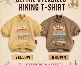 May include: Two oversized t-shirts in yellow and brown, featuring a ribbed crew neck and a graphic print of mountains and trees with the text Hiking is always a GOOD IDEA. Each shirt has a small red tag on the side and a metal snap button at the hem.