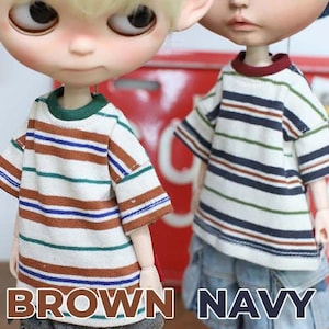 May include: Two dolls wearing striped t-shirts. One shirt has brown, blue, and green stripes on a white background, with a green collar. The other shirt has navy, brown, and green stripes on a white background, with a burgundy collar. The text "BROWN NAVY" is at the bottom.