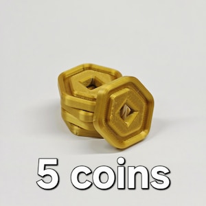 May include: A stack of five gold-colored, geometric coins with a central diamond-shaped cutout. The coins are stacked on a white surface, with the text "5 coins" in white below.