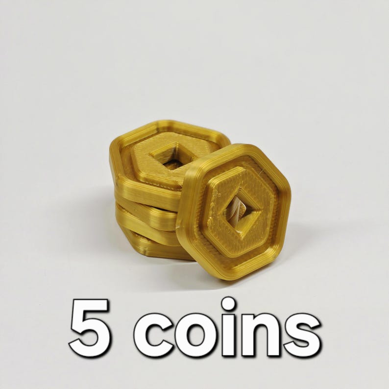 May include: A stack of five gold-colored, geometric coins with a central diamond-shaped cutout. The coins are stacked on a white surface, with the text "5 coins" in white below.