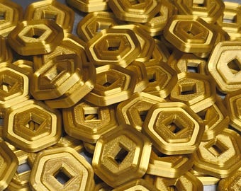 May include: A pile of gold-colored, geometric objects with a hexagonal outer shape and a square center hole. The objects have a layered design and appear to be made of a metallic material. The objects are scattered across a surface.