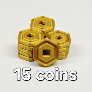 May include: Gold-colored, hexagonal coins with a square center hole are stacked in groups. The image shows 15 coins in total. The coins have a textured surface and are arranged on a white background. The text "15 coins" is displayed below the coins.