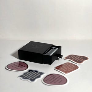May include: A black box with a drawer that opens to reveal a set of affirmation cards. The cards are printed with inspirational quotes in a variety of colors and fonts. The box is labeled "My Choice Words" and "Journal & Affirmations".