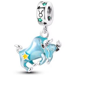 Puede incluir: Encanto de plata con un toro de esmalte azul, el signo del zodíaco Tauro, con una estrella de esmalte verde y el símbolo de Tauro en el anillo superior.