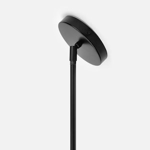 Può includere: Un apparecchio di illuminazione a soffitto nero con una calotta rotonda e uno stelo cilindrico dritto. La calotta è montata a soffitto e lo stelo si estende verso il basso. L'apparecchio è in metallo e ha una finitura opaca.