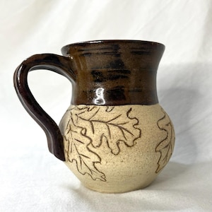 Peut inclure: Une tasse en céramique brune et crème avec une anse. La tasse est décorée d'un motif de feuilles de chêne.