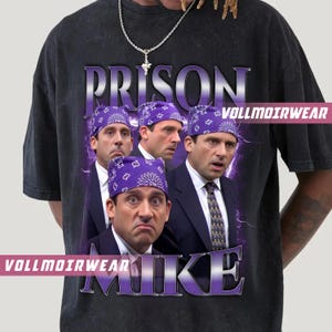May include: Dark gray t-shirt featuring a graphic of a man wearing a purple bandana, with the word "PRISON" above and "MIKE" below. The shirt has the text "VOLLMOIRWEAR" on it.