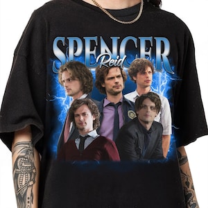Puede incluir: Camiseta negra con un estampado gráfico de cuatro hombres de la serie de televisión Mentes Criminales. El gráfico presenta el texto "Spencer Reid" y rayos.