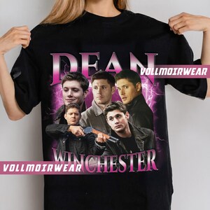 Puede incluir: Camiseta negra con un gr&aacute;fico rosa de las palabras "Dean Winchester" y un collage de cuatro hombres. Los hombres llevan chaquetas y tienen el pelo oscuro. El gr&aacute;fico est&aacute; rodeado de rayos rosas.