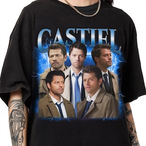 Puede incluir: Camiseta negra con un estampado gráfico de los personajes de la serie de televisión "Supernatural" con la palabra "Castiel" en letras azules arriba.