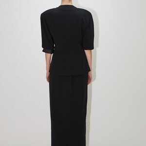 May include: A black short-sleeved blazer with a skirt, both made of a smooth, textured fabric. The blazer has a slightly fitted silhouette and the skirt is a straight, midi length.
