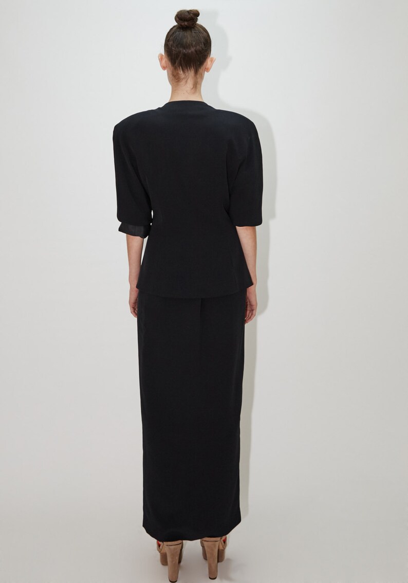 May include: A black short-sleeved blazer with a skirt, both made of a smooth, textured fabric. The blazer has a slightly fitted silhouette and the skirt is a straight, midi length.