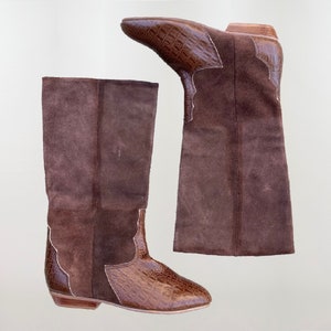 May include: A pair of brown suede knee-high boots with a crocodile-embossed leather toe and heel. The boots have a pointed toe and a low heel.