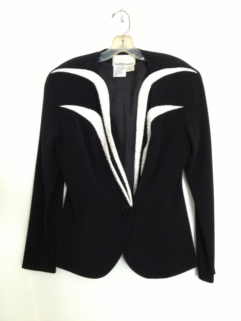 May include: A black blazer with white trim on the front and sleeves. The blazer has a single button closure.