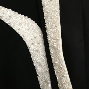 May include: Black fabric with two white beaded trim details. The beads are a mix of small round pearls and tiny white beads.