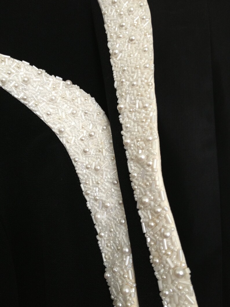 May include: Black fabric with two white beaded trim details. The beads are a mix of small round pearls and tiny white beads.